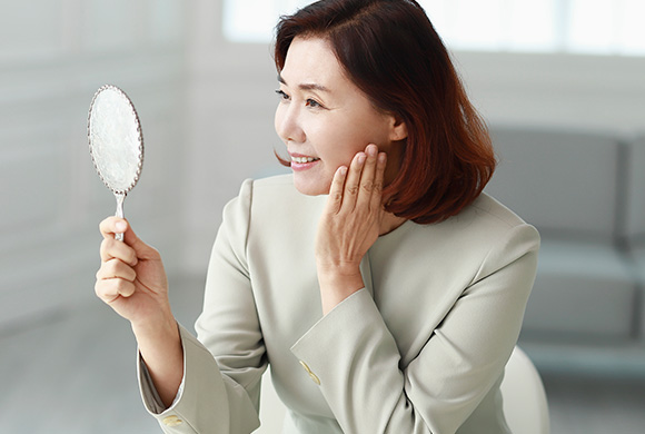 중년 여성이 손거울 보고 있는 사진